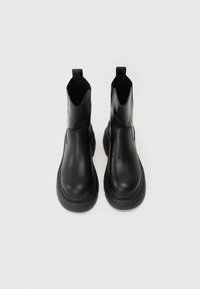 Botas de tornozelo em couro preto com um acabamento liso, bico arredondado, painéis laterais elásticos e alças para facilitar o calçar. Sola em borracha para melhor aderência.