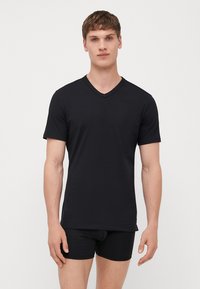 T-shirt noir à col en V fabriqué en tissu lisse ; manches courtes et coupe décontractée, porté avec un short boxer noir assorti. Design simple et minimaliste.