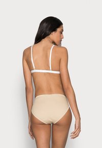 Beige lingerie set with delicate white straps, featuring a soft, smooth texture and a mid-rise brief with minimalistic design and stitching details.