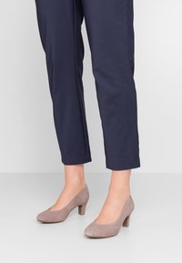 Chaussures à talons hauts en daim gris clair avec un bout arrondi et un petit talon carré, associées à un pantalon ajusté bleu marine.