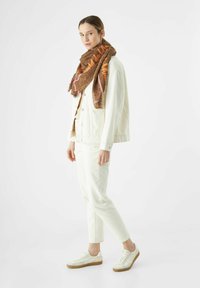 Giacca di jeans chiara e pantaloni abbinati a una sciarpa leopardata marrone con testo arancione e bordi rosa, indossata con sneakers bianche.