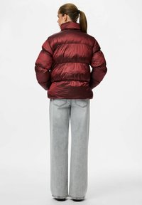 Bordo pūkuota striukė su aukštu apykaklės, horizontaliu siuvinėjimo raštu ir blizgiu paviršiumi. Derinama su šviesiai pilkais plačiakaviais džinsais.