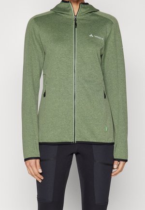 Green full-zip outdoor jacket with hood and logo on left chest, worn with black athletic pants, front view from neck to hips.