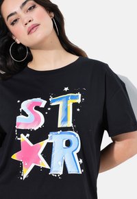 Camiseta de algodón negra con estampado colorido y audaz que dice "ST★R" en rosa, azul y amarillo, con acentos de estrellas y un corte casual.