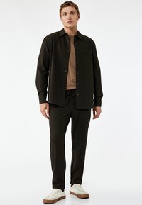 Donkere gestreepte longsleeve blouse met een zak, gecombineerd met bijpassende broek met elastische tailleband en lichtgekleurde sneakers. Glad stoftextuur.