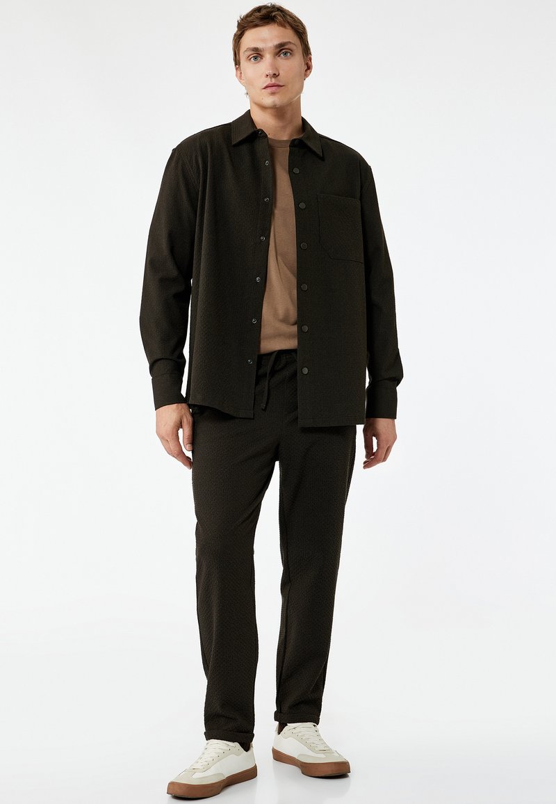 Donkere gestreepte longsleeve blouse met een zak, gecombineerd met bijpassende broek met elastische tailleband en lichtgekleurde sneakers. Glad stoftextuur.