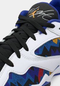 Sneaker bianca con lacci neri, motivi zigzag blu e multicolore, foderatura blu e linguetta nera con logo Jumpman giallo e firma.
