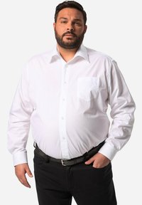 Camicia bianca a maniche lunghe con colletto a punta e taschino, abbinata a pantaloni neri e una cintura nera, caratterizzata da una texture liscia.