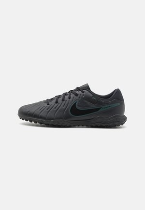 Chaussures de football noires avec une tige synthétique texturée, un bout rond et une semelle extérieure en caoutchouc noire. Présence d'un logo Nike vert et de la marque "Tiempo".