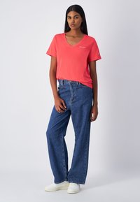 T-shirt corallo con scollo a V e maniche corte, abbinato a jeans larghi in denim blu a vita alta. Sneakers bianche completano l'outfit.