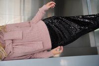 Rosa gerippter Pullover mit langen Ärmeln und umgeschlagenem Kragen, kombiniert mit einem schwarzen Paillettenrock mit wellenförmigem Muster.