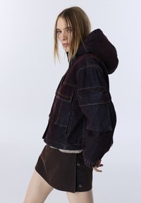 Džíny kabát, tmavě burgundský s kapucí, s mnoha kapsami a manžetami; spojený s hnědou mini sukni.