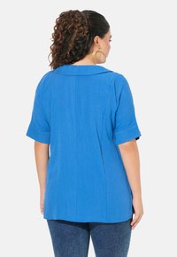 Camicia blu a maniche corte con colletto a punta, realizzata in tessuto testurizzato. Presenta una vestibilità comoda e un orlo curvo sul retro.