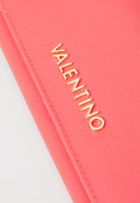 Koralju teksturēta maka ar zelta "VALENTINO" logo, ar gludu apdari un iestiprinātiem malām. Kompakta taisnstūra forma.
