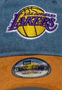 Casquette de baseball en denim bleu avec un logo des Los Angeles Lakers brodé en jaune et violet, avec une visière en suède marron et une sangle réglable.