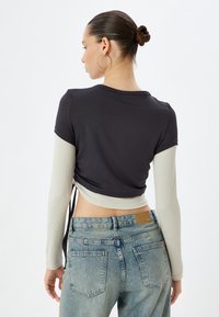 Zwart shirt met korte mouwen en lange crèmekleurige mouwen, aansluitende pasvorm, gestructureerde stof en verstelbare zijstrik, gecombineerd met lichtblauwe jeans met hoge taille.