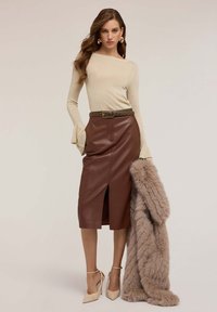 Maglione beige a maniche lunghe, gonna midi in pelle marrone con spacco frontale, cintura marrone con borchie e scialle beige soffice; tacchi alti beige.