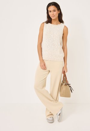 Light knit sleeveless top in cream, fitted at the waist. Paired with beige wide-leg pants and gray sneakers. Carrying a small beige bag.