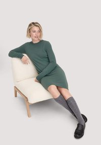 Strickkleid in Grün, mit langen Ärmeln, endet oberhalb der Knie. Passt zu knielangen grauen Socken und schwarzen Mokassins mit Fransen.