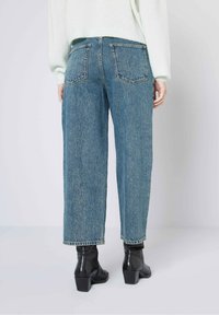 Hooglopende, wijd gesneden jeans in lichtblauwe denim, voorzien van een klassiek vijf-pocket ontwerp en gestikte achterzakken, gecombineerd met zwarte enkelboots.