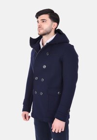 Cappotto doppiopetto blu navy con grandi bottoni neri, cappuccio e tasche laterali, caratterizzato da una vestibilità strutturata e una trama liscia simile alla lana.