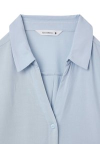 Camicia azzurro chiaro a maniche corte con colletto, dotata di chiusura con bottoni e una piccola tasca sul petto. Realizzata in tessuto liscio. Taglia S.