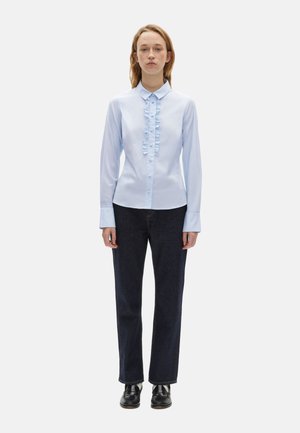 Himmelblaues Hemd mit Knopfleiste und Rüschendetails in der Mitte, kombiniert mit dunklen Denim-Jeans im geraden Schnitt. Einfacher Kragen und lange Ärmel.