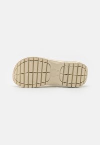 Light beige sneaker sole with a patterned rubber outsole, featuring a mix of textured sections and grooves for traction.