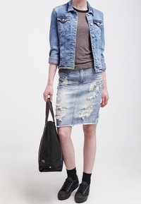 Jeansjacka med uppvikt ärm och fickor med lock, grå T-shirt, trasig denim blyertskjol, svarta sneakers och en svart tote-väska.