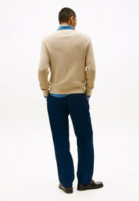 Beżowy sweter z splotu, z dekoltem w kształcie V i dżinsowym kołnierzykiem, w połączeniu z granatowymi spodniami i ciemnym obuwiem, widziany z tyłu.