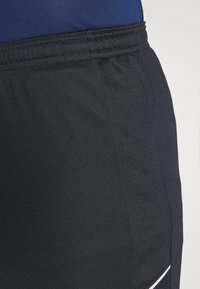 Shorts sportivi neri realizzati in tessuto liscio e testurizzato con un pannello in rete. Una striscia bianca di dettaglio corre lungo la cucitura laterale.