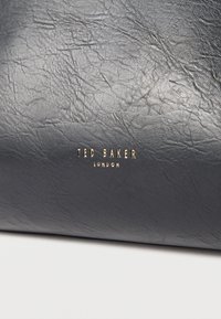 Υλικό από υφή δέρματος σε ναυτικό μπλε με εμφανές σχέδιο κόκκου. Χρυσό λογότυπο "Ted Baker London" τοποθετημένο κεντρικά στο κάτω μέρος.