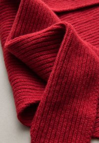 Sciarpa rossa lavorata a maglia con trama a coste e materiale in lana morbida. Il tessuto è piegato, evidenziando il suo calore e spessore.