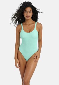 Un maillot de bain une pièce vert menthe avec des bretelles fines, un décolleté rond et un tissu texturé présentant des ondulations subtiles. Ouvertures de jambe haute.