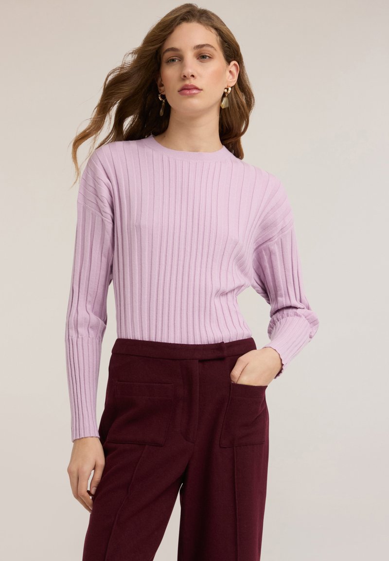 Maglione viola chiaro a coste con maniche lunghe e scollo tondo. Abbinato a pantaloni a vita alta di colore bordeaux scuro con tasche.