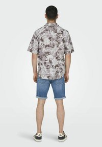 Kurzärmliges Hemd mit floralem Muster in Mauve- und Weißtönen, kombiniert mit hochgekrempelten Jeansshorts und schwarz-weißen Sneakers.