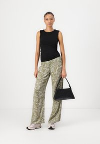Black fitted tank top, olive-green loose floral print pants, and a black handbag with a logo, paired with light pink athletic shoes.