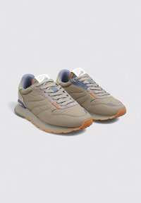 Baskets de sport beige avec une finition texturée, accents gris et détails oranges. Dotées de lacets et d'une languette rembourrée pour un confort supplémentaire.