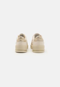 Un paio di sneakers Skechers beige viste da dietro, con suole beige e pannelli del tallone accentati in oro, su sfondo bianco.