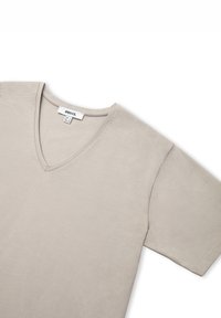 Camiseta de algodón suave de manga corta en color beige con un diseño de cuello en V y costuras cuidadas a lo largo de los bordes.