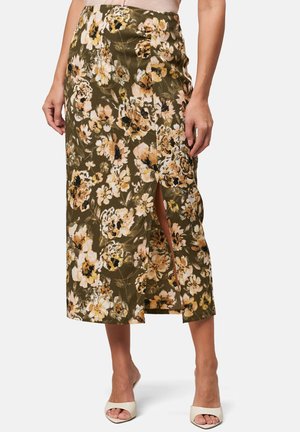 Jupe midi florale en vert olive avec un tissu texturé, présentant des fleurs jaunes et noires, une fente sur le côté et une taille ajustée.