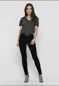 T-shirt cinza com decote em v combinado com jeans skinny pretos e botas de tornozelo estampadas. O conjunto apresenta uma silhueta ajustada e texturas subtis.