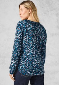 Langärmlige Bluse mit einem blau-schwarzen geometrischen Muster, ausgestattet mit einem elastischen Ausschnitt und gerafften Ärmeln, aus leichtem Stoff gefertigt.