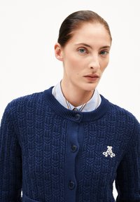 Navy gestrickte Strickjacke mit einem strukturierten Muster, Rundhalsausschnitt und Knopfverschluss. Inklusive eines kleinen gestickten Logos auf der linken Brust.