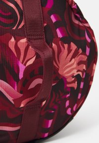 Close-up van een kleurrijke, gemusterde stof met tinten rood en roze, met donkere accenten en een opvallende, gestructureerde band.