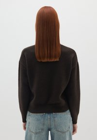Dunkelbrauner, strukturierter Pullover mit lockerer Passform, überschnittenen Schultern und gerippten Bündchen, kombiniert mit hellblauen, hochtaillierten Jeans.