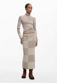 Beige ribbed knit sweater with a mock neck, paired with a matching long skirt featuring horizontal stripes. Worn with brown ankle boots.