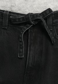 Čierne denims nohavice s opaskom na viazanie a jemným štruktúrovaním. Majú pútka na opasok a rovný predný strih. Tkanina má hladký, matný povrch.