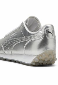 Sneaker metallizato argento con un design elegante, caratterizzato da una texture rigata, lacci bianchi e una suola puntinata per una migliore aderenza. Marchio Puma sul lato.