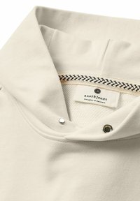 Maglione beige con collo a imbuto, tessuto strutturato, dettagli con bottoni a pressione e etichetta interna con accento tessuto.